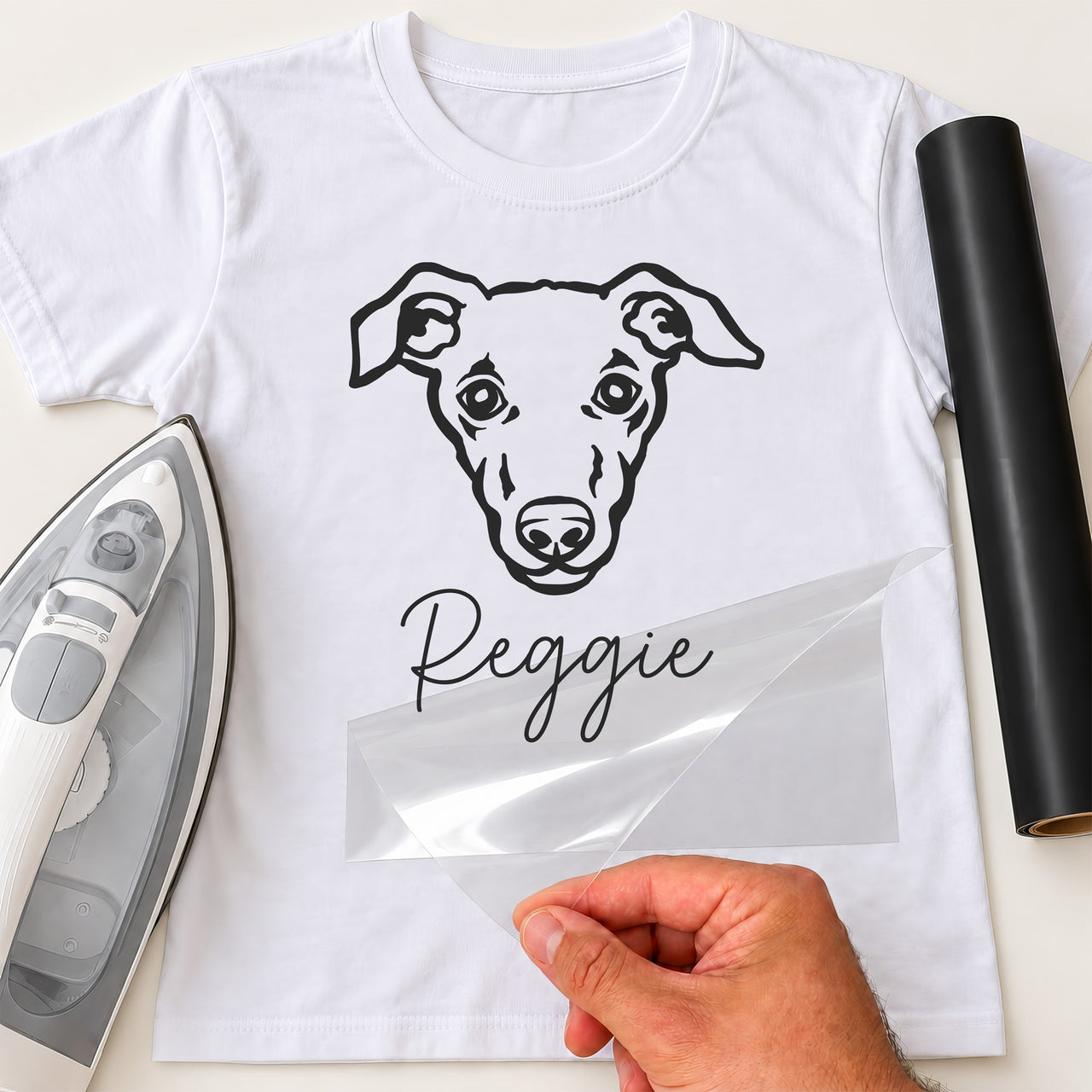 White T-shirt with black line-art dog face and script name 'Reggie', personalised pet iron-on transfer, iron and vinyl roll
