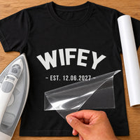 Wifey date iron-on transfer: white WIFEY EST. 12.06.2027 on a black T-shirt, film being peeled