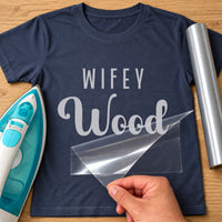 Navy tee mockup with silver vinyl 'Wifey' above the script surname 'Wood', clear film being lifted away