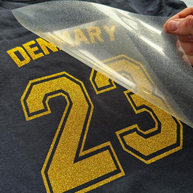 Clear sheet peeled off a gold glitter DENMARY 23 on a navy T-shirt