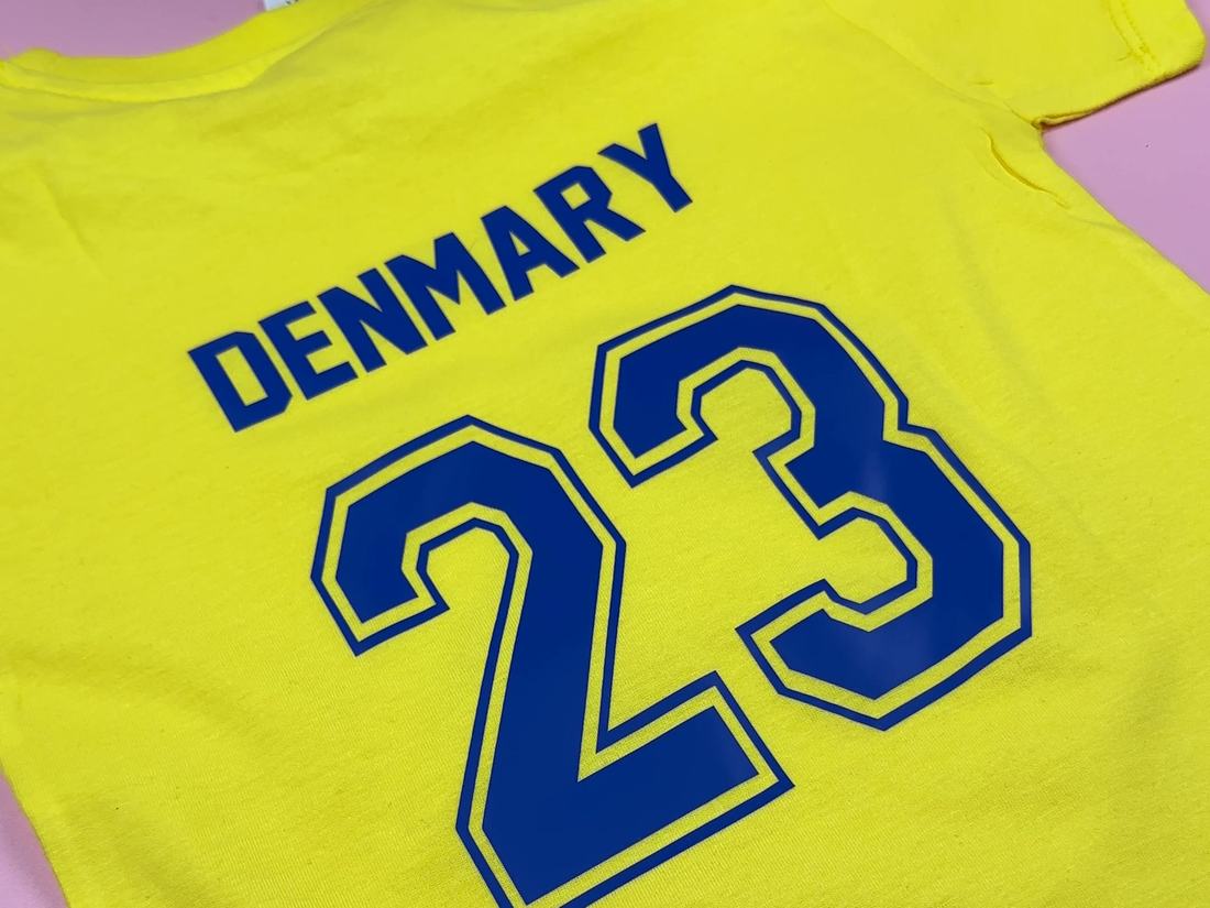 Close-up of a yellow kids T-shirt with DENMARY and number 23 in royal blue iron-on vinyl, just pressed