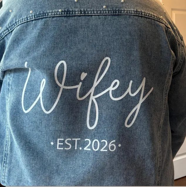 Back of a denim jacket with Wifey EST. 2026 in white matte vinyl, buyer's photo